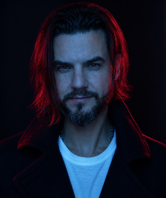 Retrato de Ric Neves, iluminado em vermelho e azul sobre fundo preto